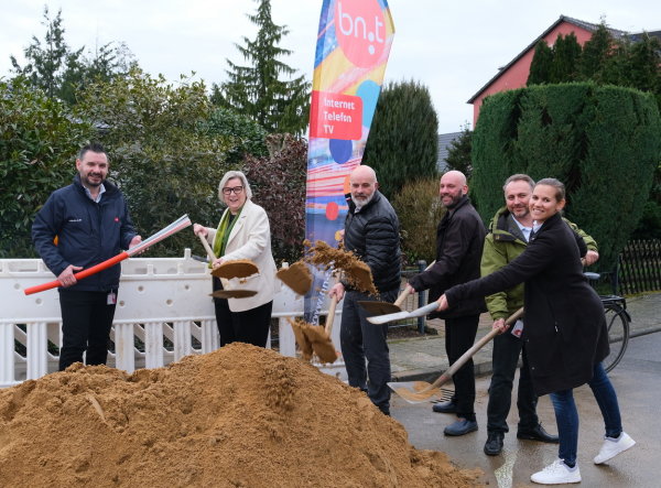 Auf dem Bild sieht man die Teilnehmer des Spatenstichs um einen Erdhügel stehend. Jeder Teilnehmer hält eine mit etwas Erde beladene Schaufel in der Hand. Auf dem Foto sind v.l.n.r.: Nikolaos Pantios -Vertriebsleiter bn:t-, Bürgermeisterin Kalkbrenner, Ortsvorsteher Norbert Sauren, Wirtschaftsförderer Martin Koenen, Lukas Romanowski -Rollout Manager bn:t-, Barbara Gardner -Leiterin Marketing bn:t-