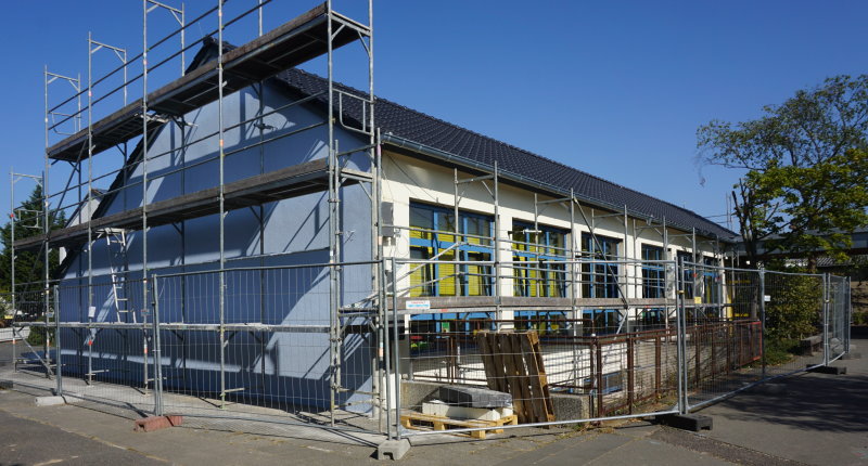 Zu sehen ist ein Baugerüst, welches derzeit am Mittelhaus der Grundschule in Buschhoven steht. Das Baugerüst geht bis an das Giebeldach, da auch dieses saniert werden muss.