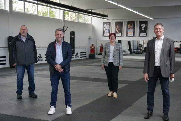 Auf dem Bild sind die Verantwortlichen des Taekwondo-Vereins und Bürgermeisterin Kalkbrenner zu sehen, die in der Turnhalle stehen und sich über die Gratulation freuen.