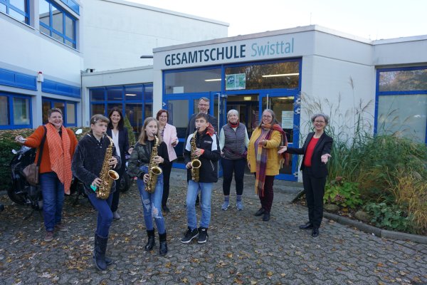 Drei Schülerinnen und Schüler sowie weitere Mitwirkende stehen vor der Gesamtschule Swisttal.