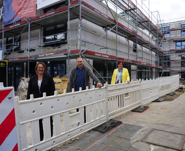 Auf dem Bild sind die Verantwortlichen für den Bau der Libento Seniorenresidenz zu sehen, die vor der Baustelle stehen. Das Haus für die Residenz ist grau eingerüstet und das Gebäude ist zudem eingezäunt.