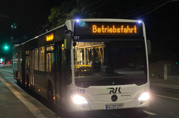 Auf dem Bild ist ein Bus in der Nacht zu sehen, der an einer Straße hält. Der Bus hat die Aufschrift 