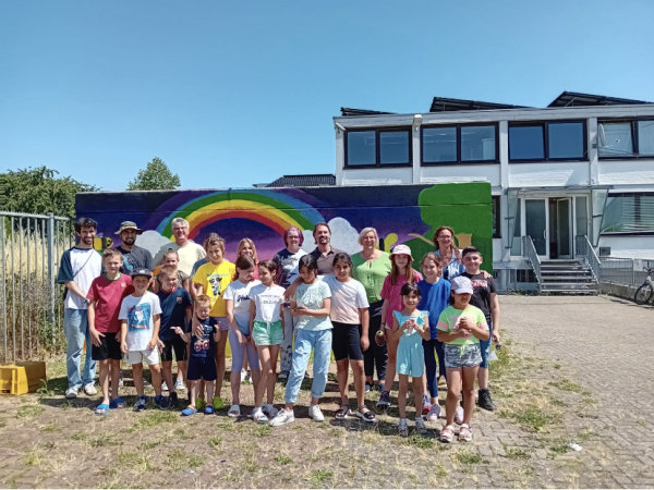 Teilnehmerinnen und Teilnehmer der Spraydays in Heimerzheim stehen vor der besprayten Wand, die sie gemeinsam erstellt haben.